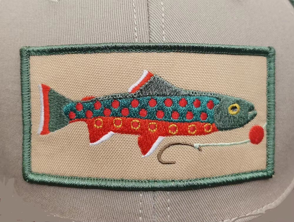 An embroidered fish patch with green border sewn onto a beige cap