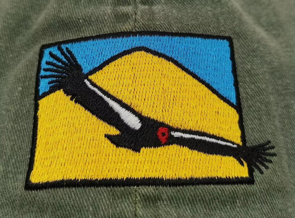 Flat embroidery on a green cap: a desert and bird scene stitched in yellow, blue and black thread