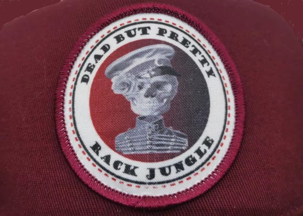 A sublimation printed round patch with photographic skull artwork and text, stitched onto a maroon cap