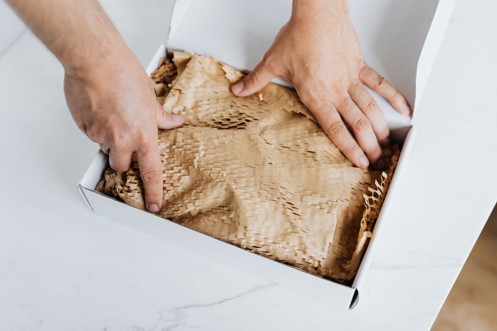 Hands folding protective paper over a small custom order inside a box before it is packed for shipping
